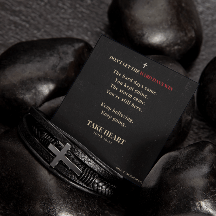 Men's black leather cross bracelet on dark stones with inspirational message card.