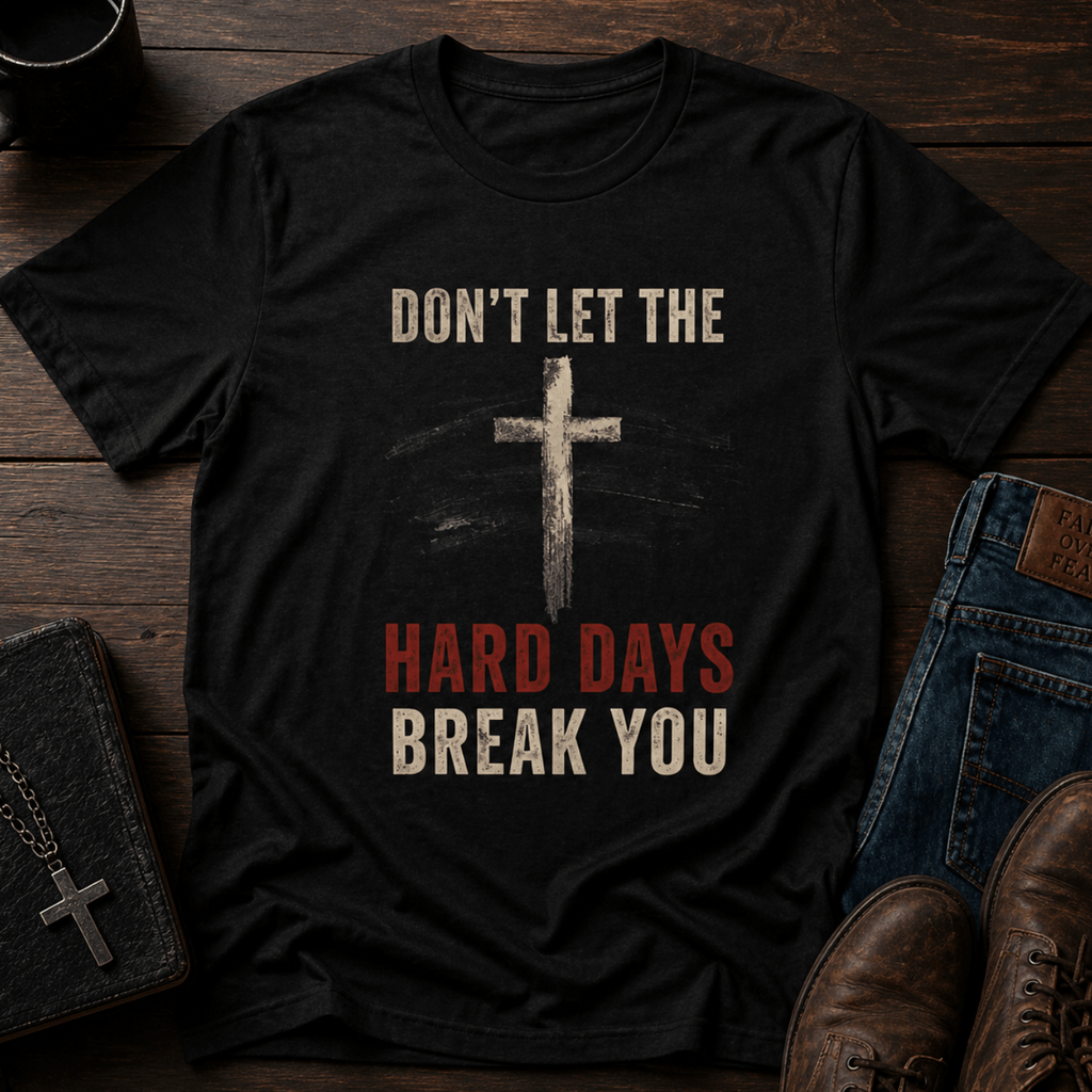 Black t-shirt with motivational quote and cross design on a wooden surface with shoes and wallet.