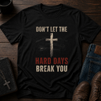 Black t-shirt with motivational quote and cross design on a wooden surface with shoes and wallet.