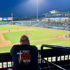 Shane, founder of Held & Anchored, wearing the Don't Let the Hard Days Win Back Print Tee at a baseball game — John 16:33
