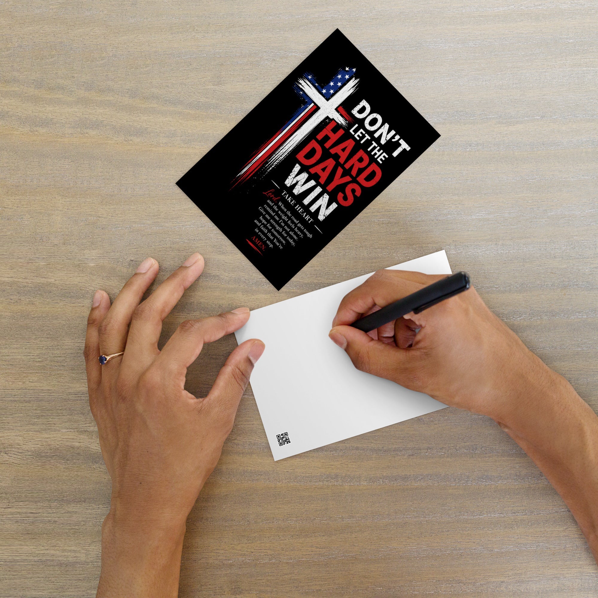 Patriotic Christian encouragement postcard with distressed American flag cross and “Don’t Let the Hard Days Win” message beside a handwritten note on a wooden table.