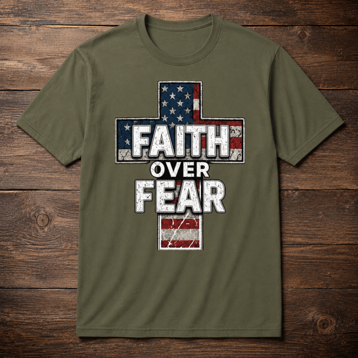 Military green t-shirt displayed in a flat lay product photo on a rustic wooden background, featuring a distressed American flag cross graphic and bold Faith Over Fear lettering on the front.