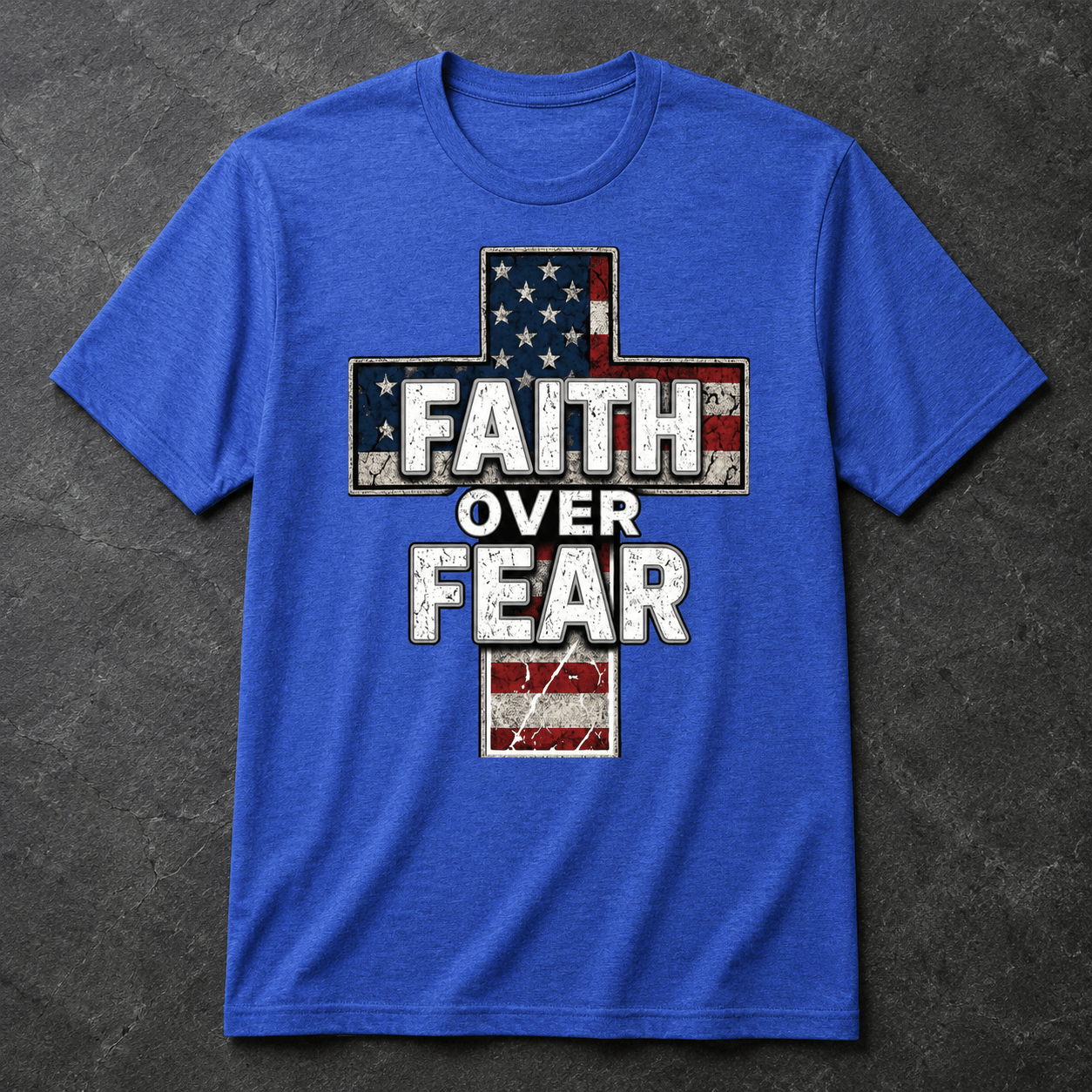 Heather true royal blue t-shirt displayed in a flat lay product photo on a dark slate textured background, featuring a distressed American flag cross graphic and bold Faith Over Fear lettering on the front.