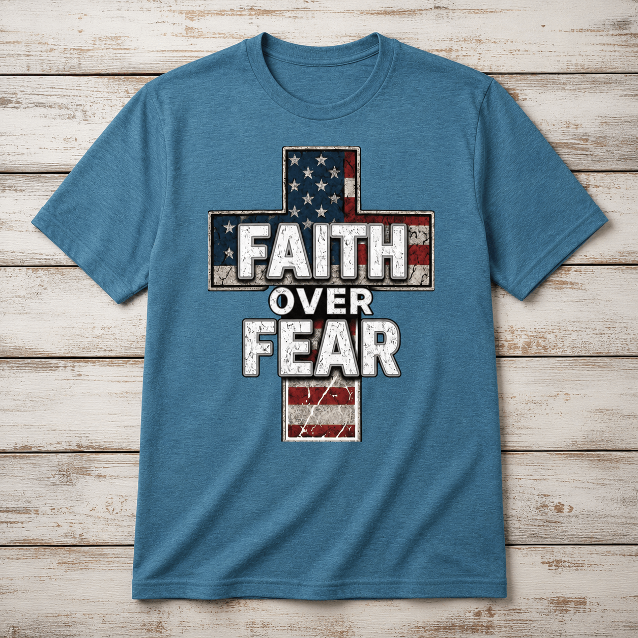Heather deep teal t-shirt displayed in a flat lay product photo on a distressed white wood background, featuring a vintage American flag cross graphic and bold Faith Over Fear lettering on the front.