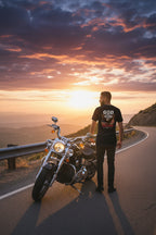 Man standing next to a motorcycle on a road with a sunset sky