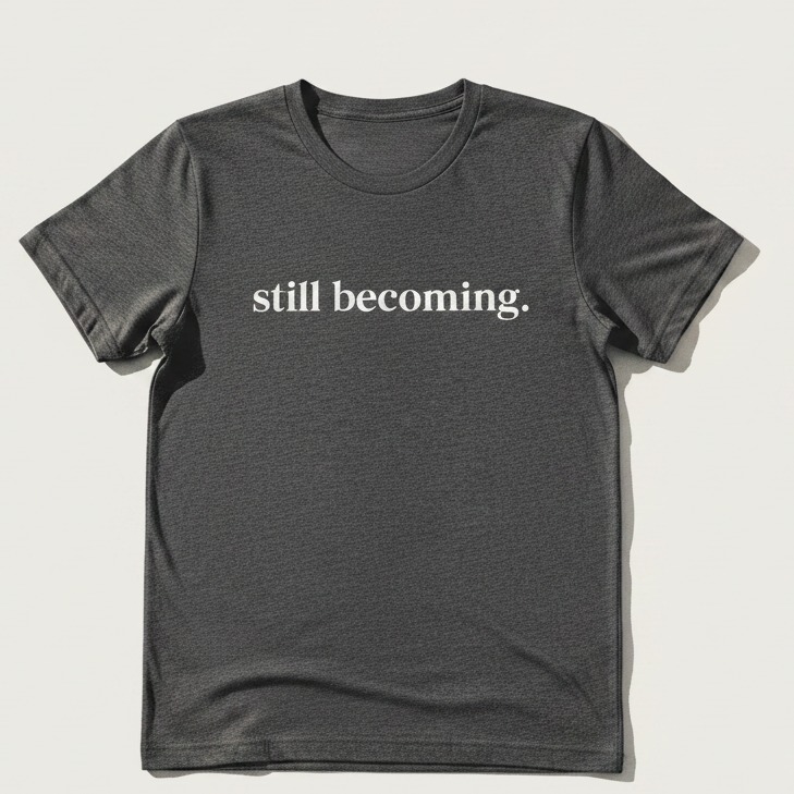Black t-shirt with 'still becoming.' text on a light background
